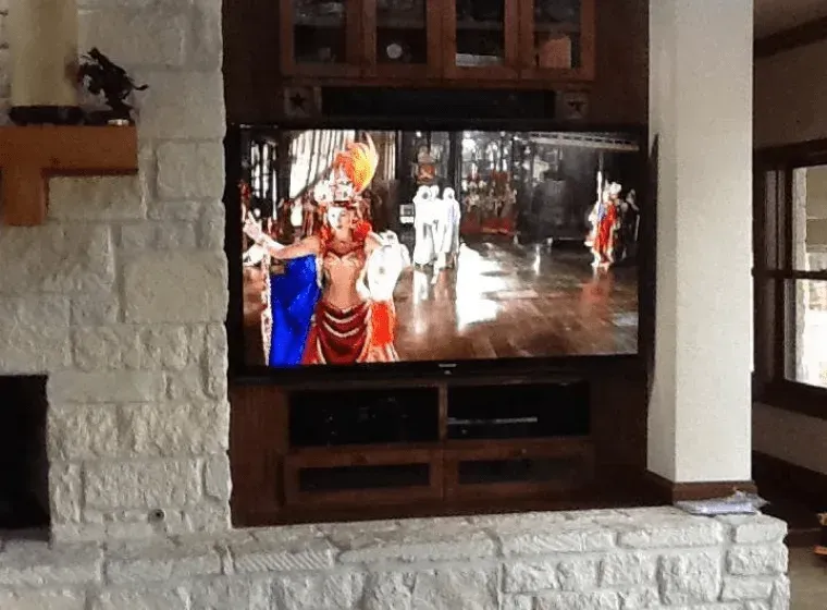 TV displaying a colorful indoor procession in a room with a stone fireplace and wood cabinet