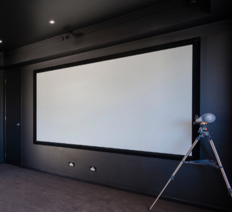 Large blank projection screen in a dark home theater room with a tripod-mounted projector on the right.