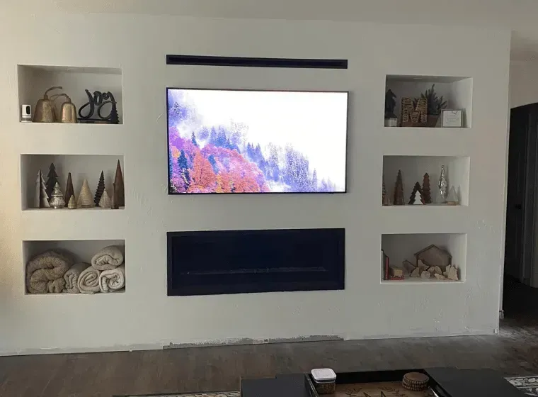 Wall-mounted TV above a black fireplace insert, flanked by decorative shelves in a modern living room.