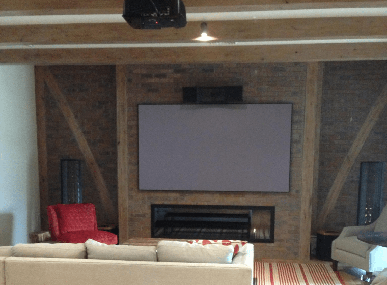 Cozy living room with a fireplace, large TV, beige sofa, red chair, and rustic wood beams