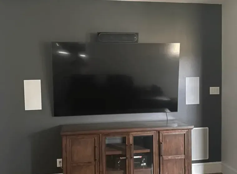 Wall-mounted TV on a dark gray wall above a wooden media cabinet with white speakers on both sides