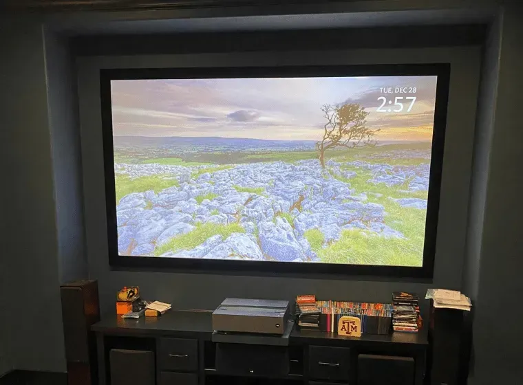 Home theater with a projector screen showing a landscape and a digital clock in a dark media room.