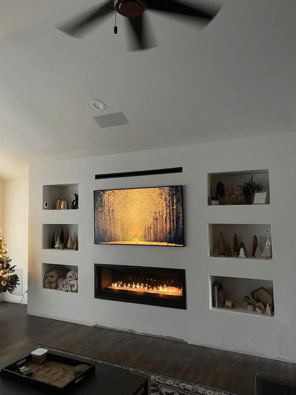 Modern living room with wall fireplace, glowing art, built-in niches, and a ceiling fan