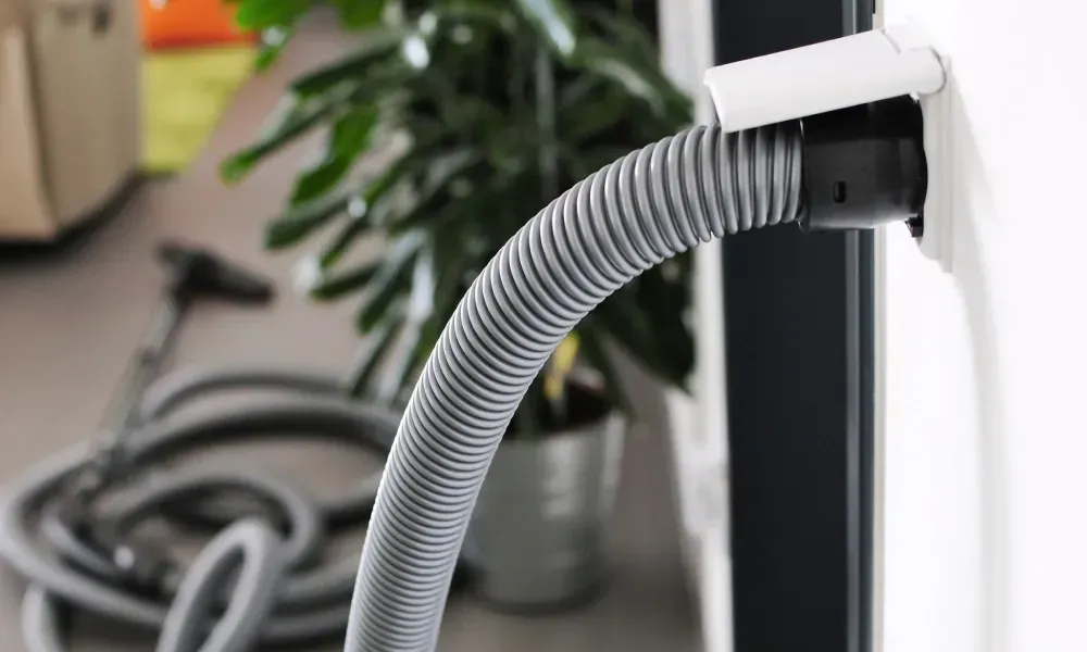 Gray corrugated vacuum hose attached to a black machine in an indoor workspace