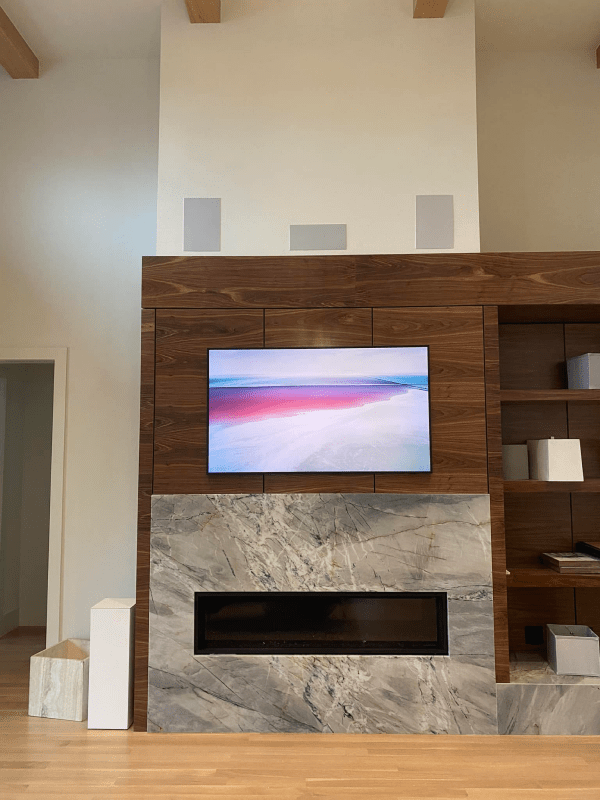 Modern living room with wall-mounted TV above a stone fireplace and built-in wood shelving.