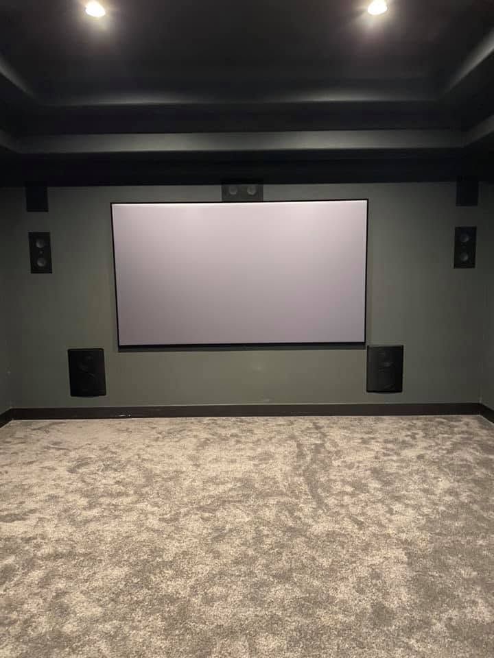 Modern home theater with projector screen, black leather seating, coffee table, and shag rug