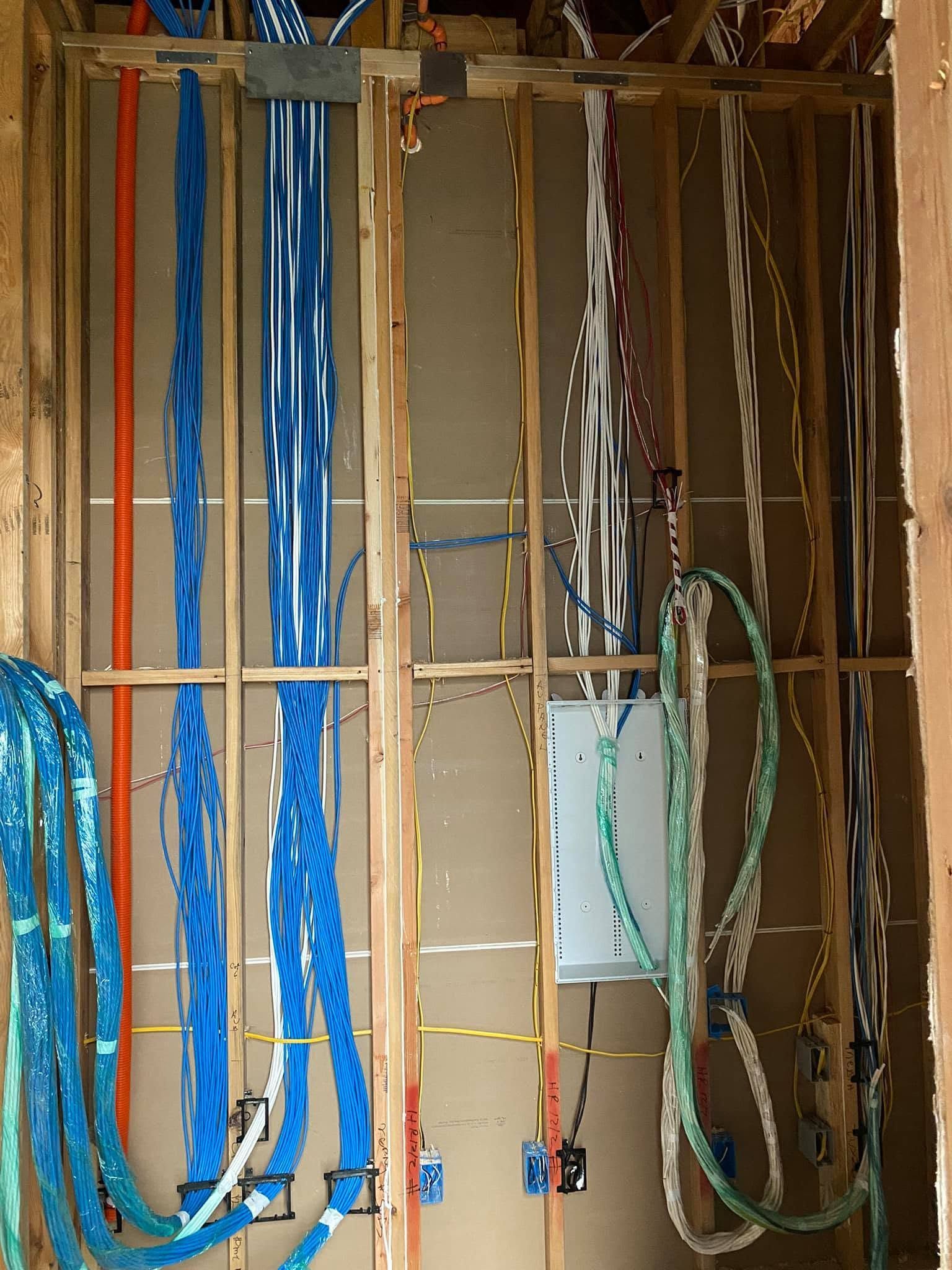 Exposed wall framing with hanging blue, green, and white electrical cables in a construction area