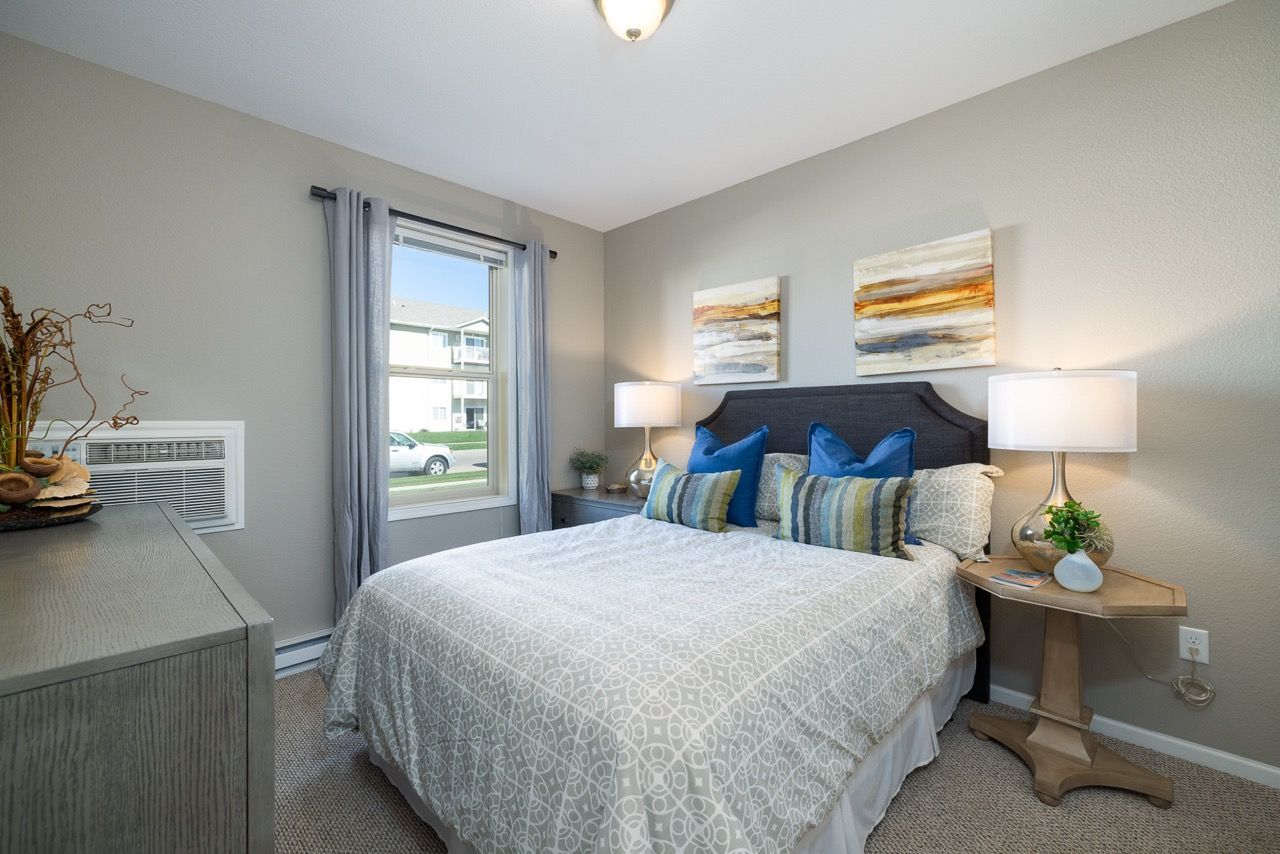 Bedroom with a queen bed, two nightstands, lamps, and a window.