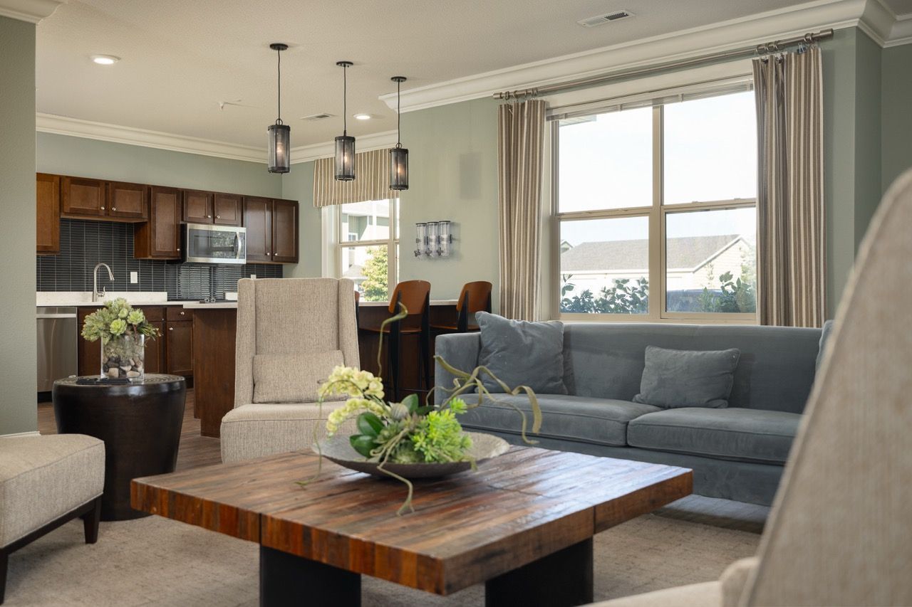 Open-concept living area with gray sofa, wooden coffee table, and a kitchen in the background.
