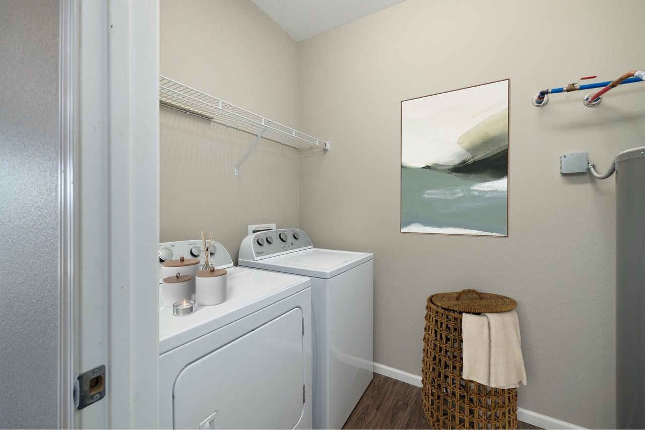 Apartment laundry room with washer and dryer, wire shelf, and woven basket.