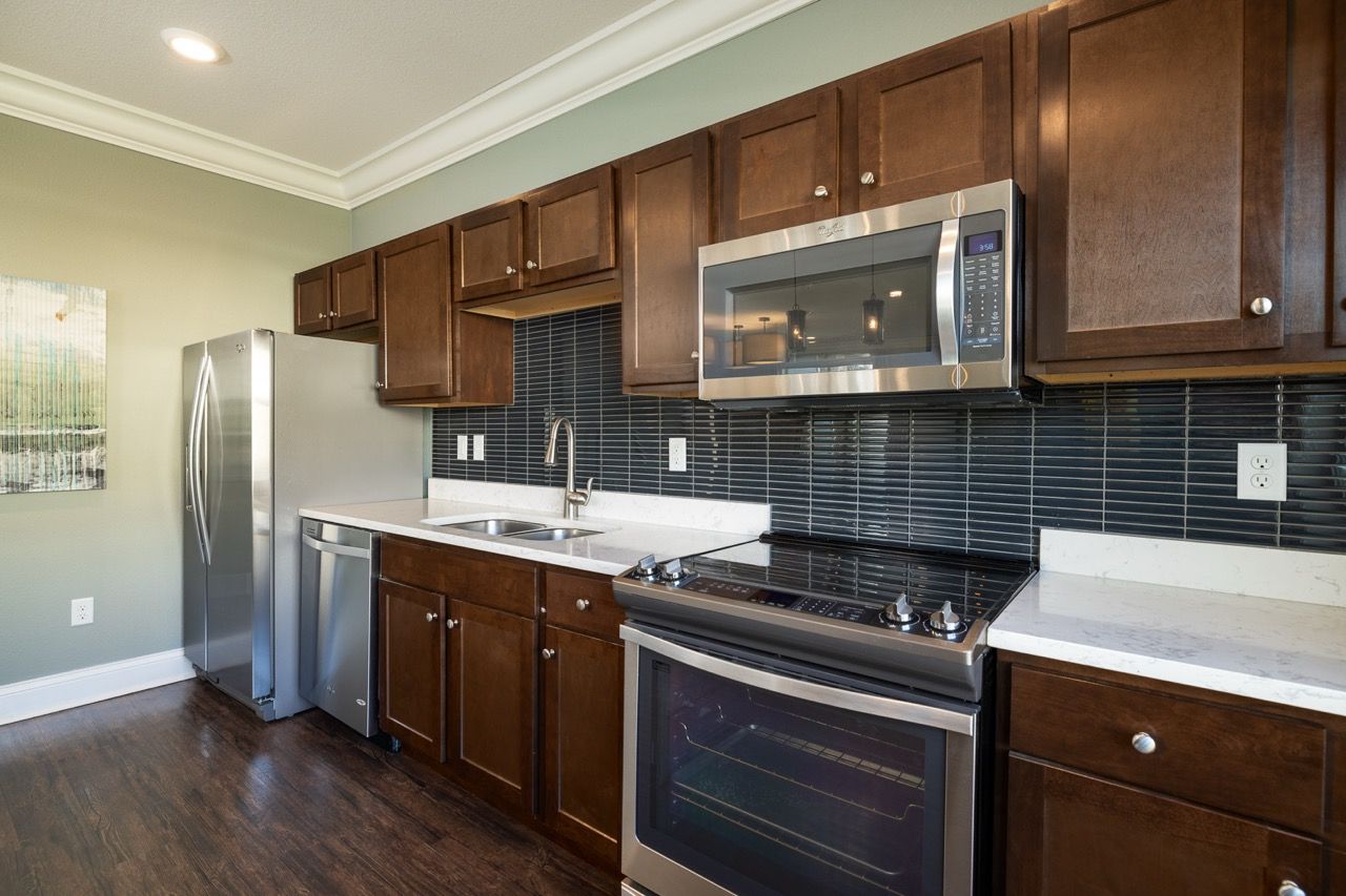 Modern kitchen with dark wood cabinets, stainless steel refrigerator, microwave, and smooth white countertops.