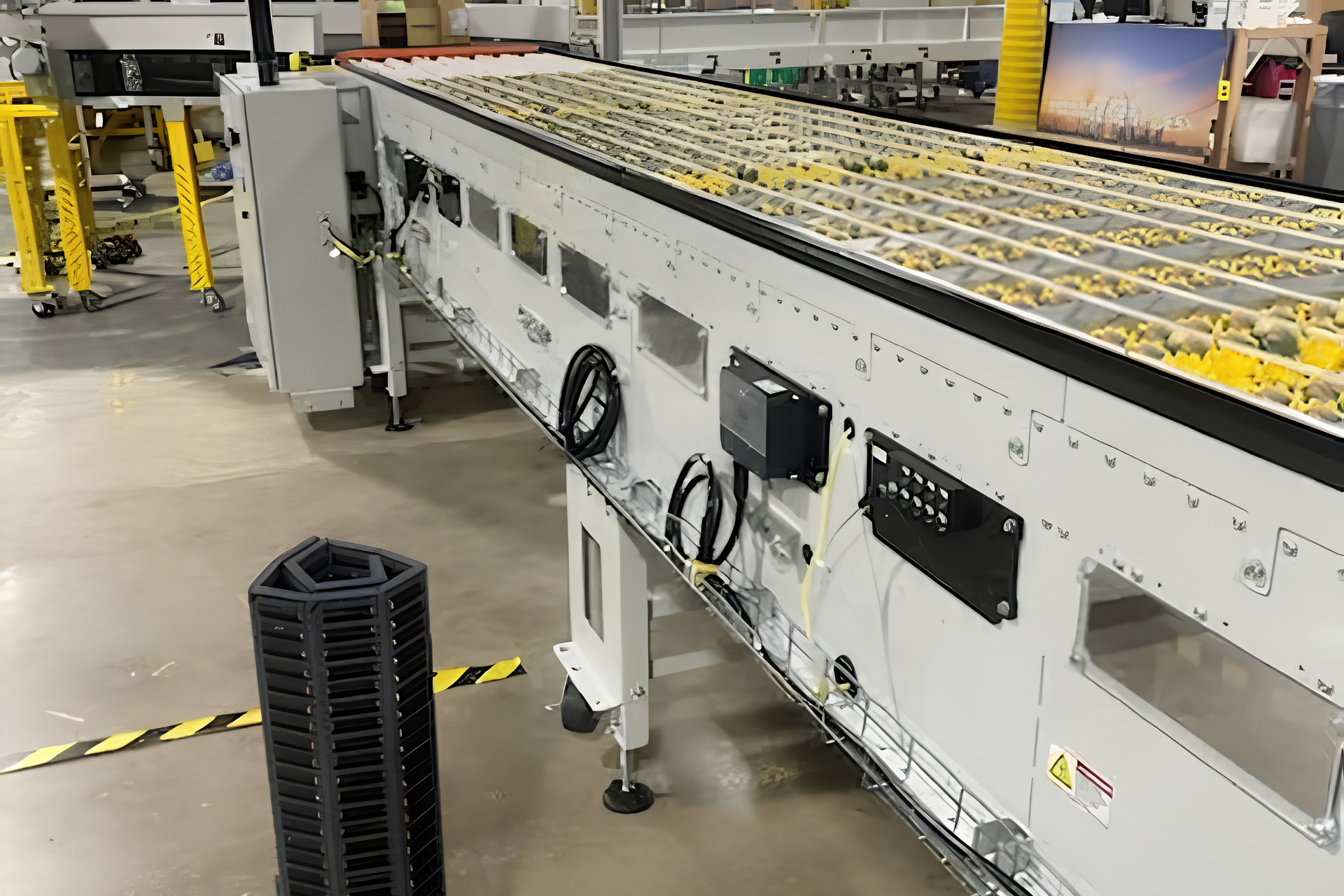 Industrial conveyor line in a factory, with yellow roller sections and control panels on a white machine.