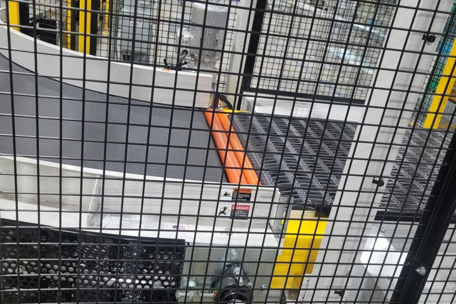 Orange package on a conveyor belt behind a black safety fence in an industrial setting