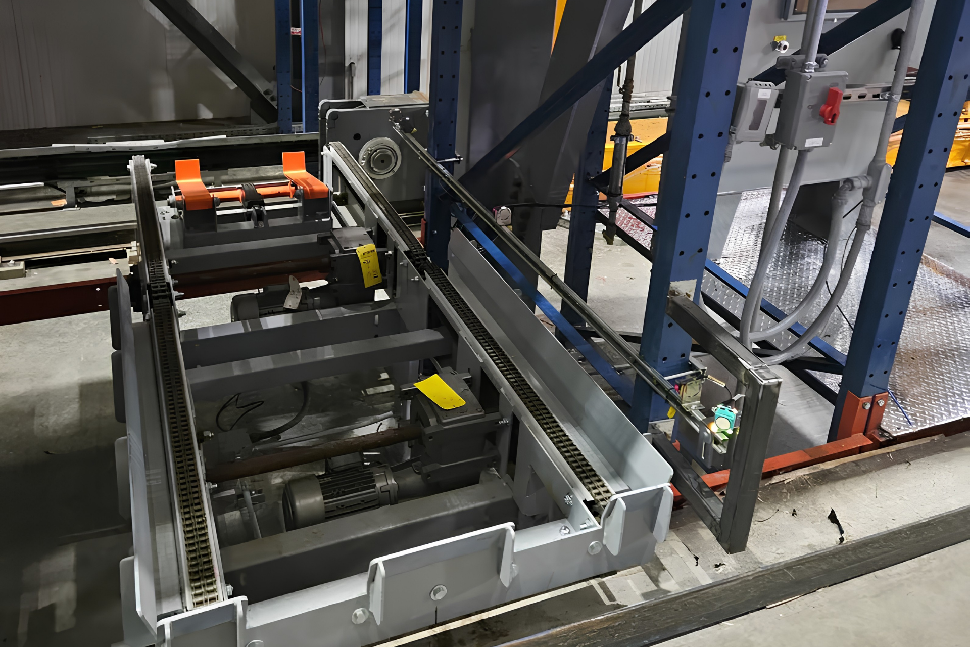Industrial machine with metal conveyor components and orange rollers in a factory setting