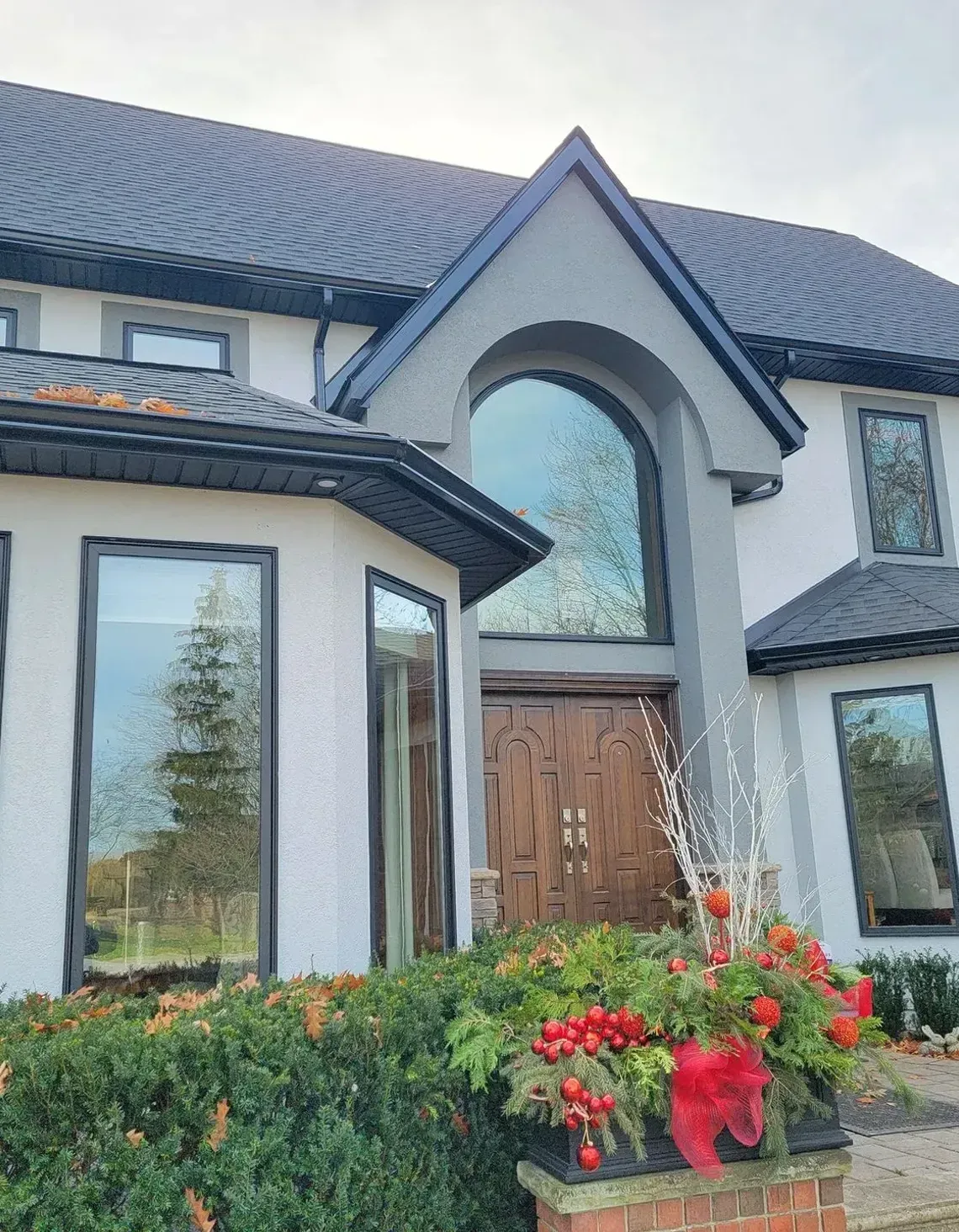 Two-story stucco home with a dark shingled roof, dark window frames, an arched front window, and a wooden double door.