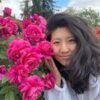 Woman with long dark hair smiles near vibrant pink peonies.