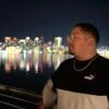A man is standing in front of a body of water at night.