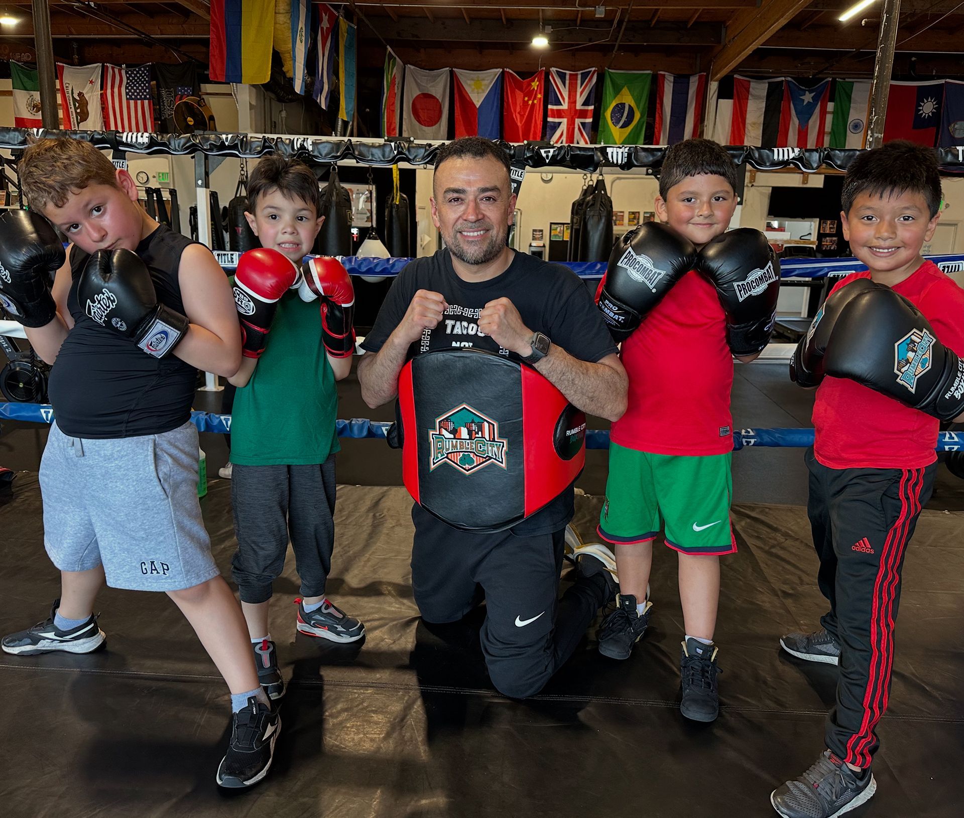A boxing instructor with four young students wearing gloves in a gym.