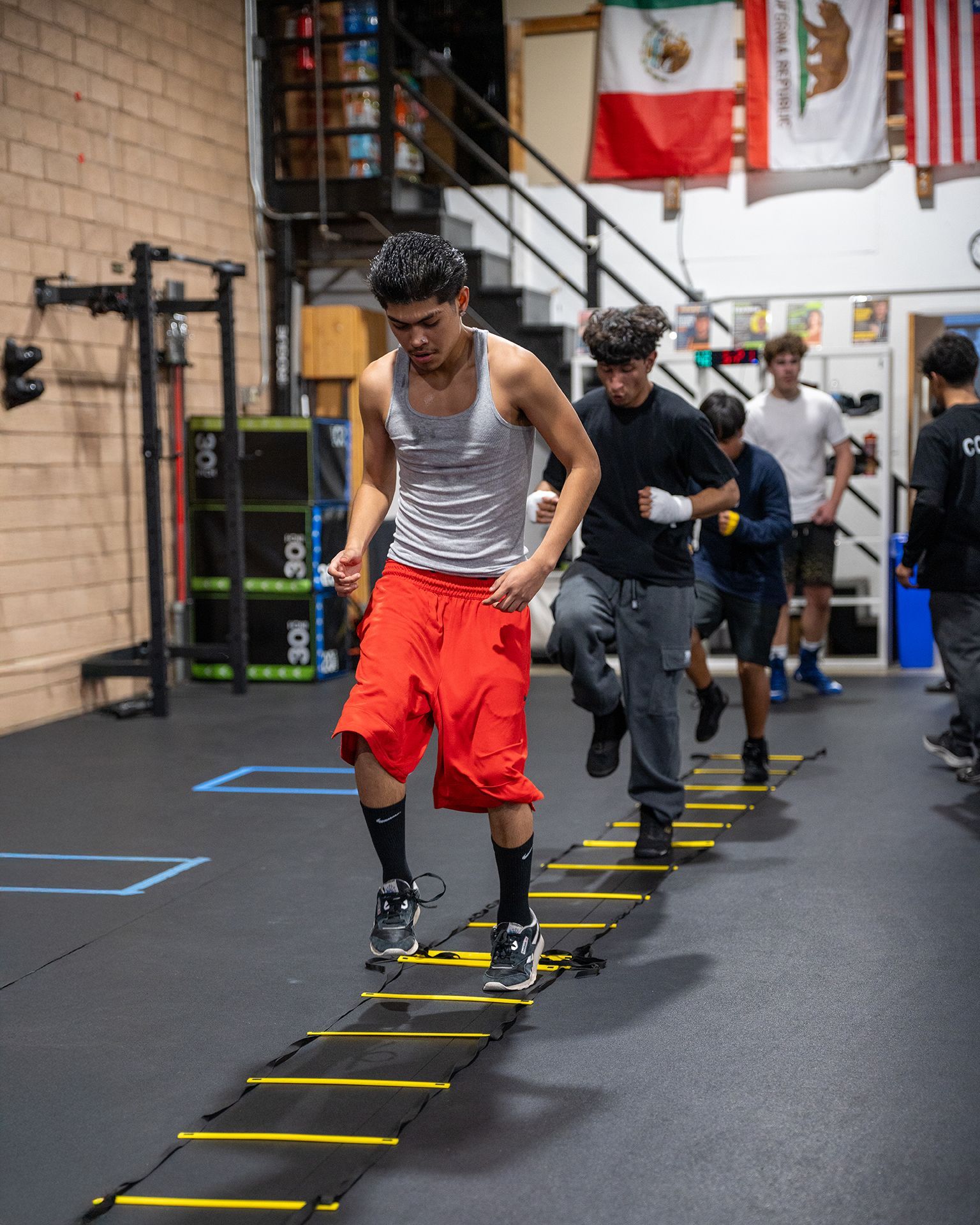 Group of young men running agility ladder drills in a boxing gym.