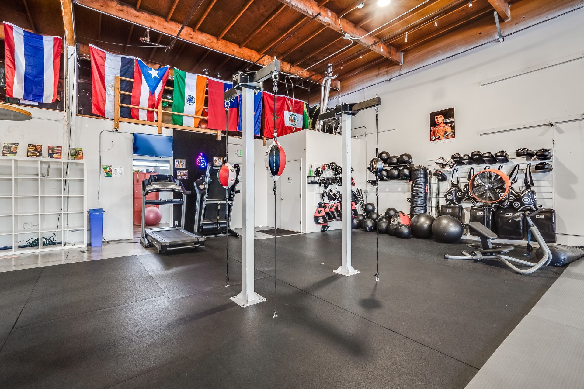 Gym interior with exercise equipment, flags, and a wooden ceiling.