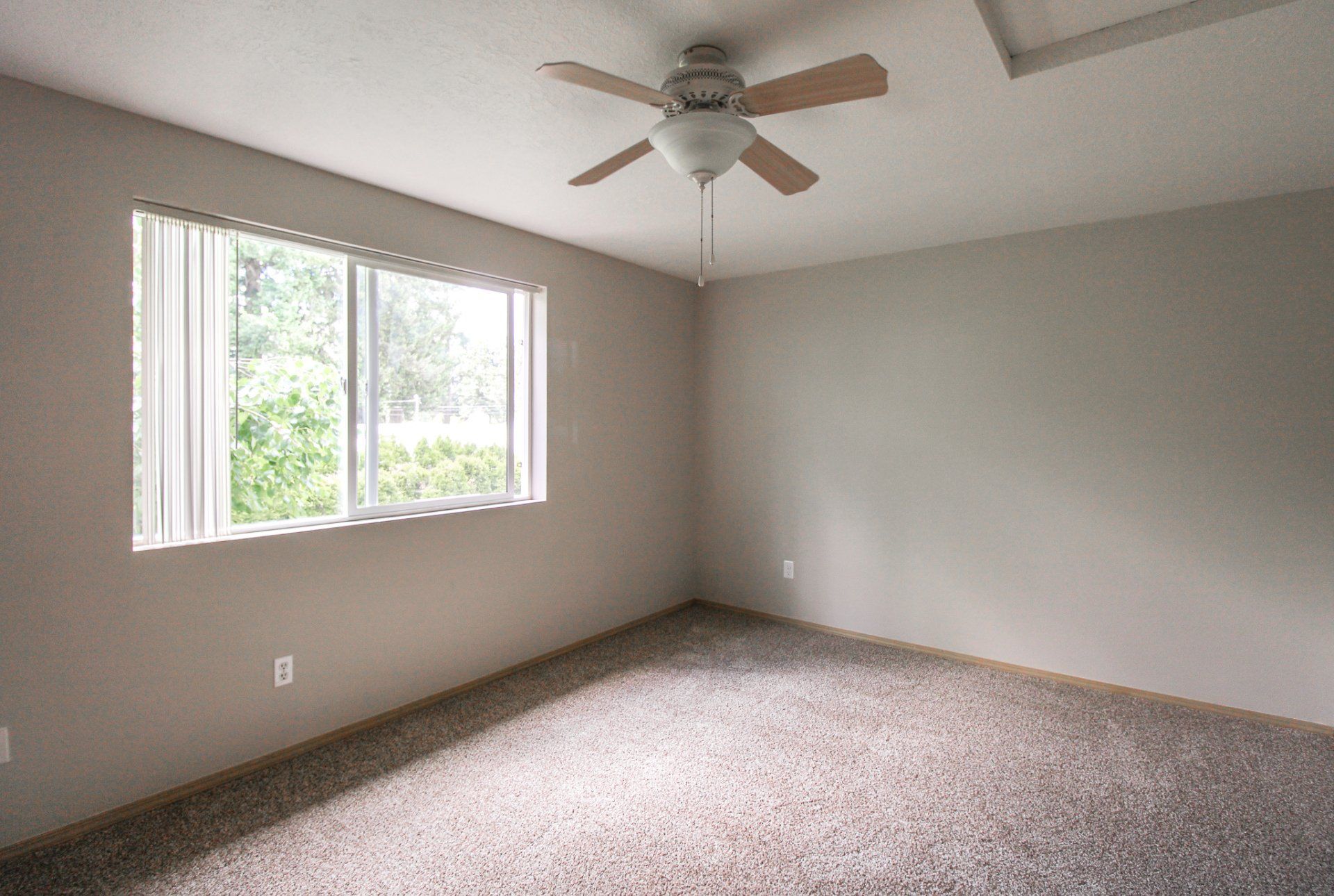 An empty bedroom with a ceiling fan and a window.