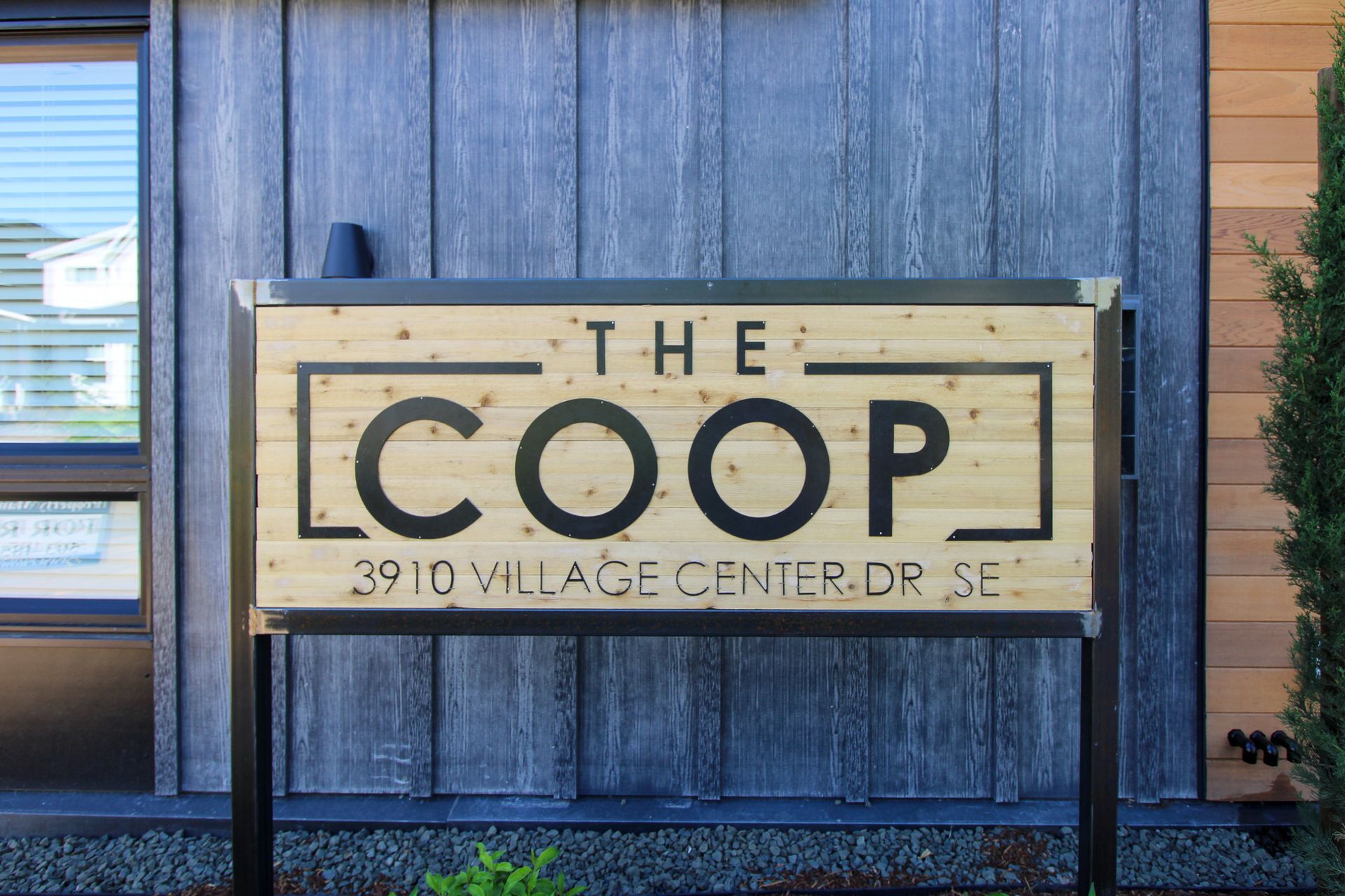 A wooden sign for the coop is on the side of a building.