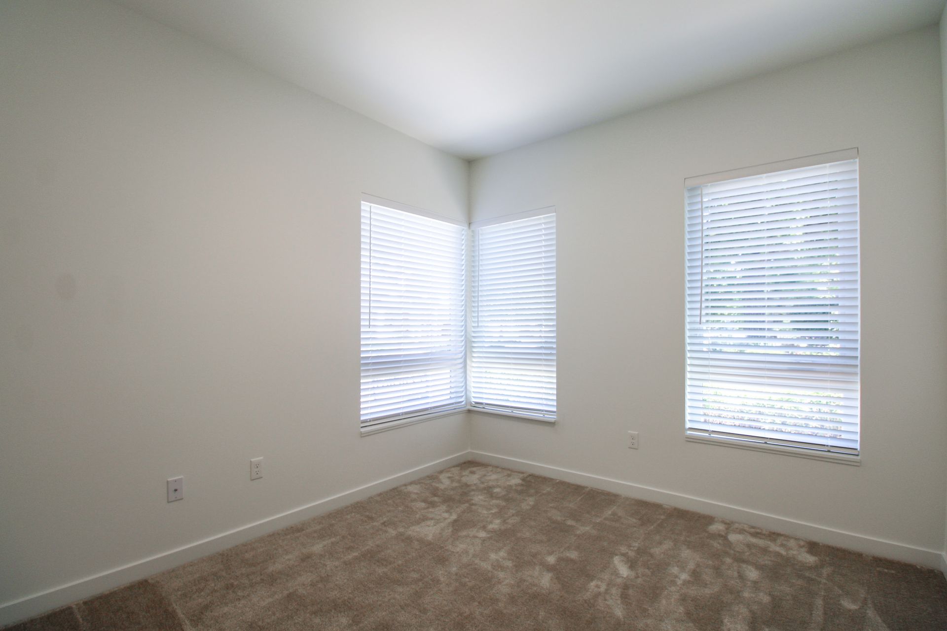 An empty bedroom with two windows and blinds.