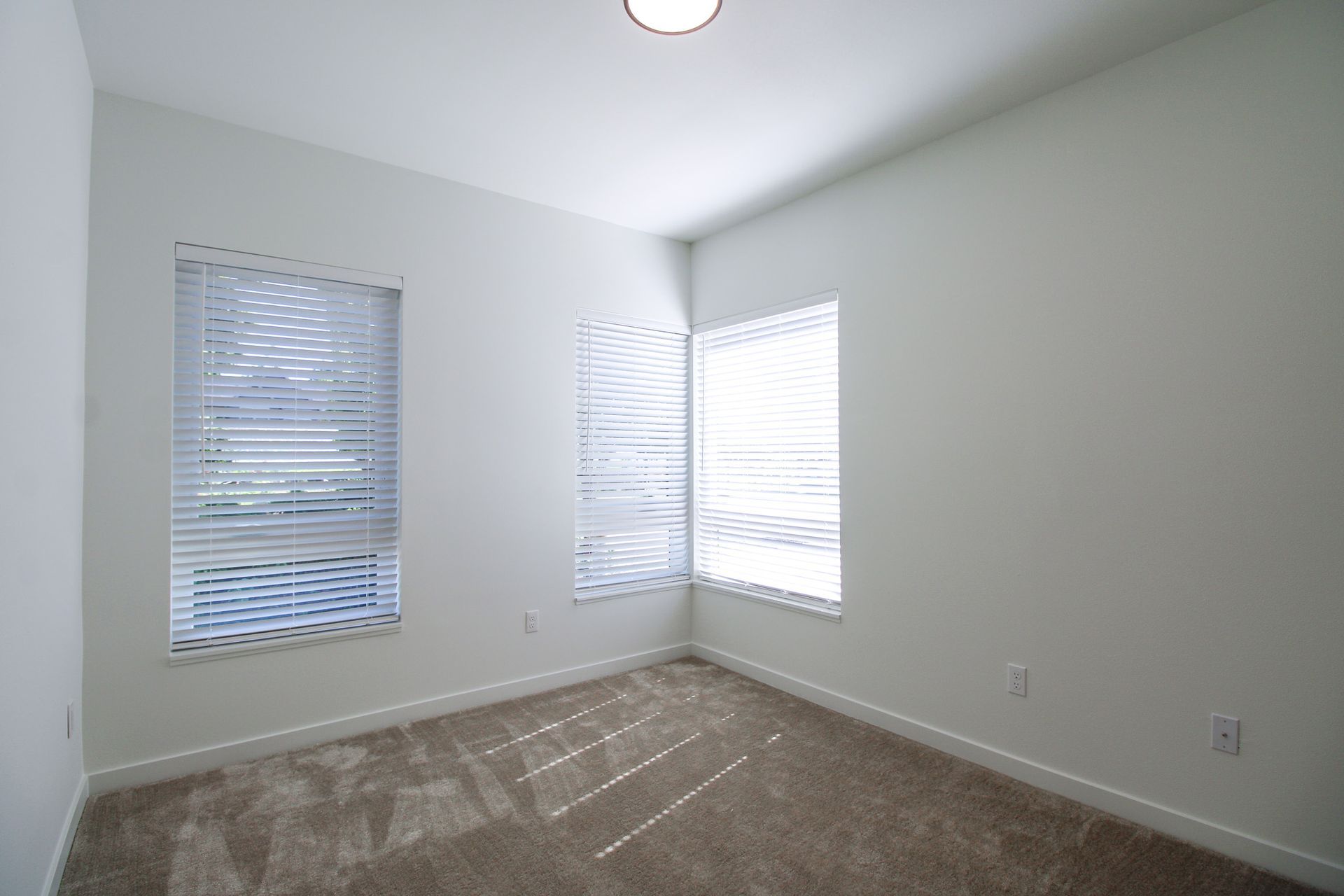 An empty bedroom with two windows and blinds on the windows.