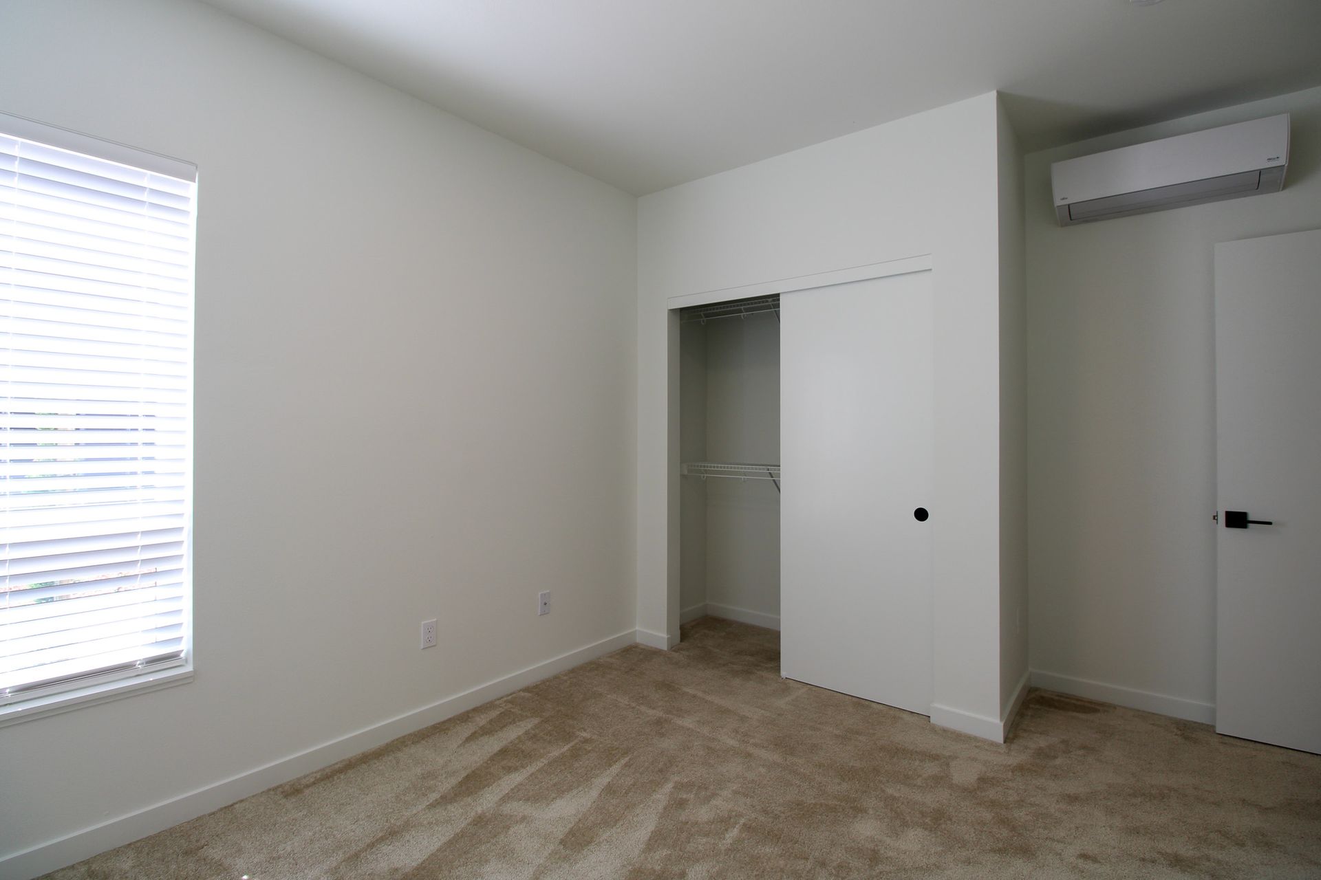 An empty bedroom with a closet and a window.