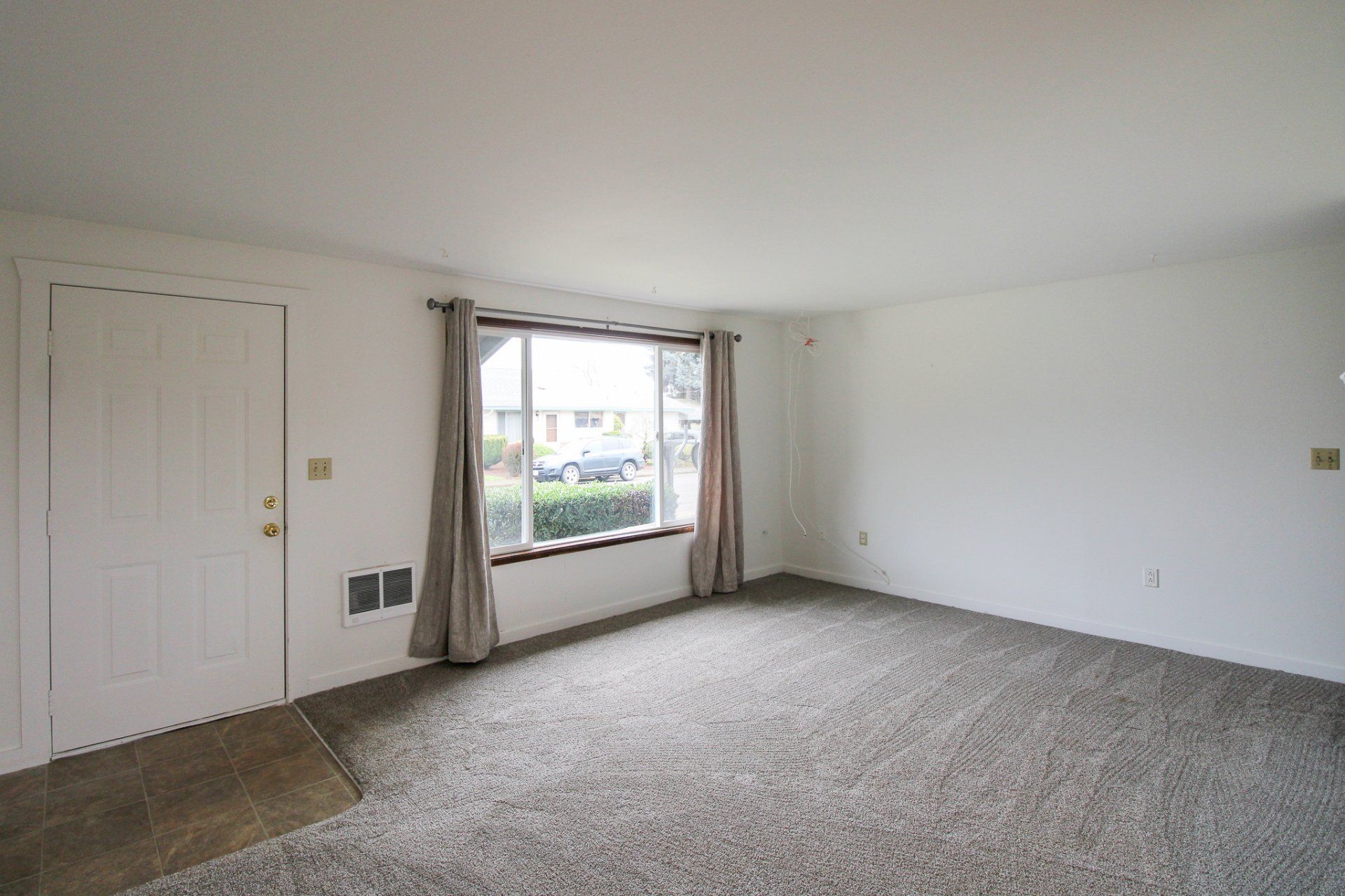 An empty living room with a large window and carpet.