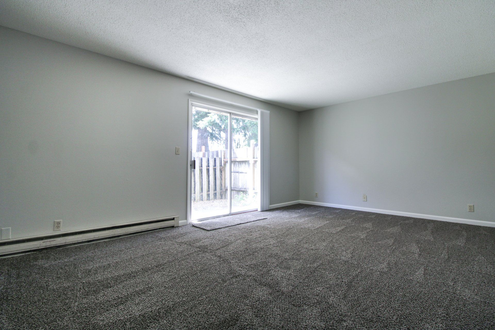 An empty living room with a sliding glass door leading to a patio.