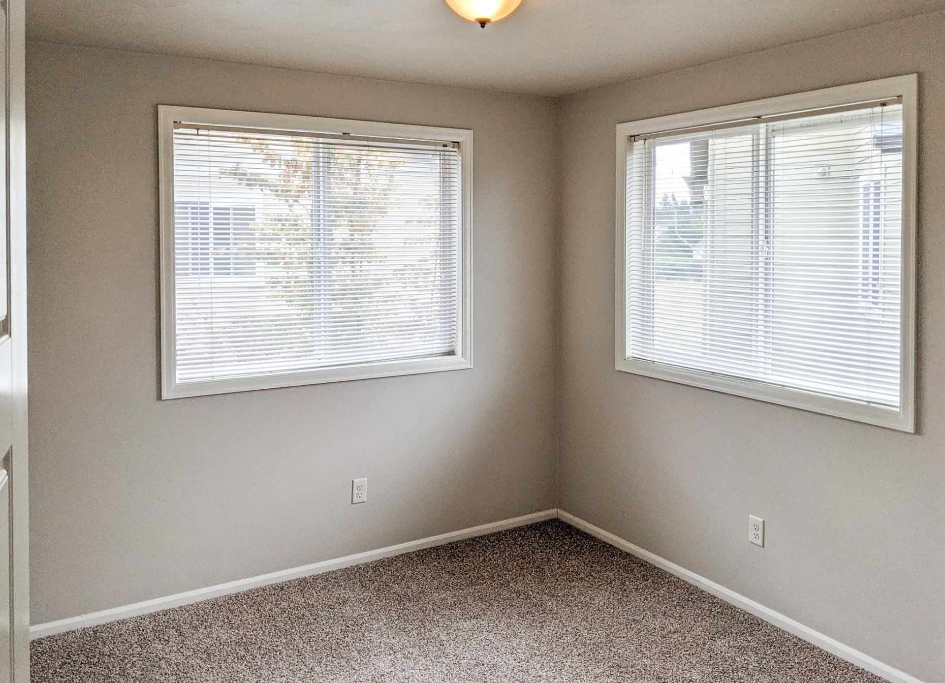 An empty room with two windows and blinds on the windows.