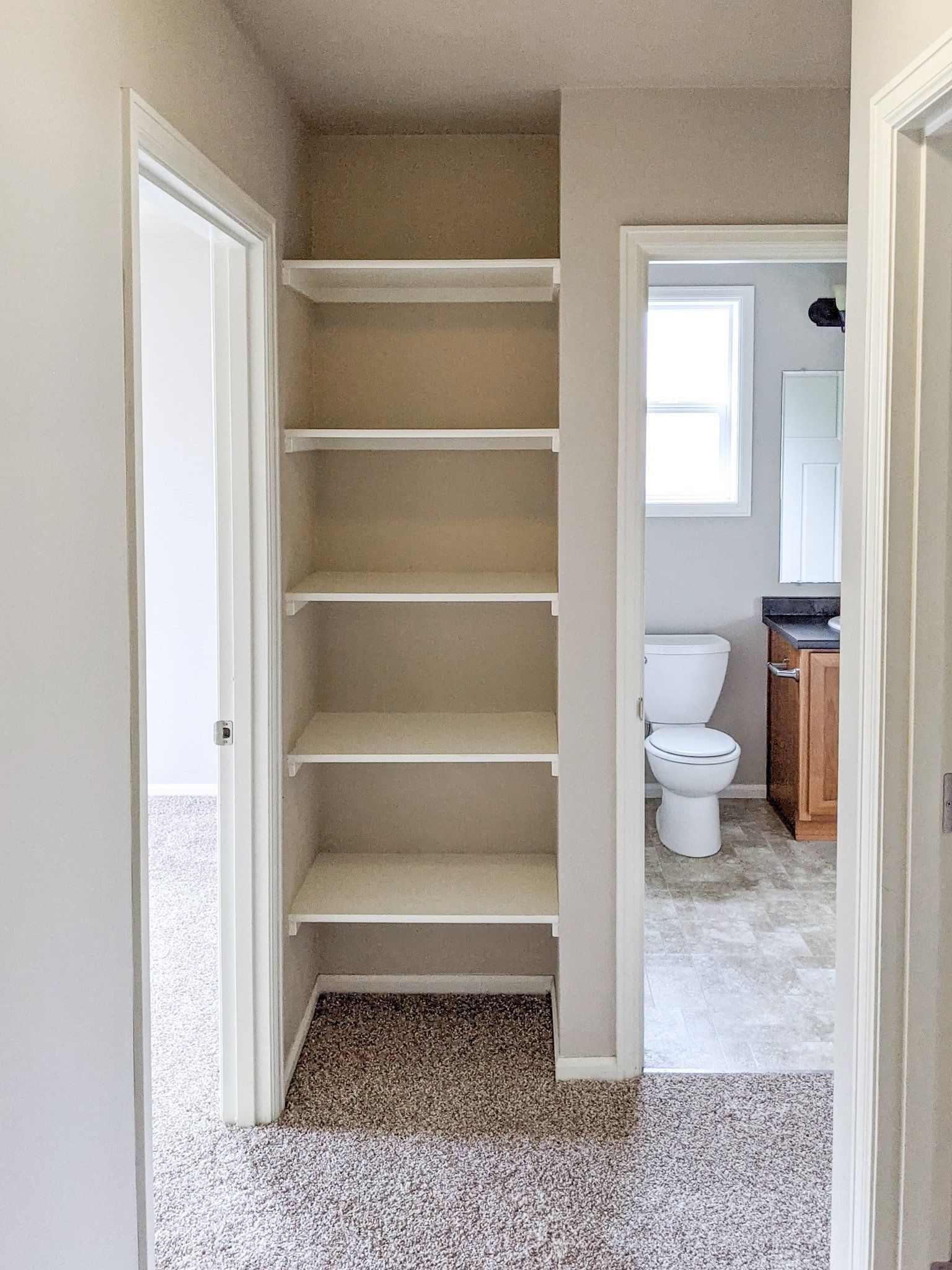 A hallway with shelves leading to a bathroom and a toilet.