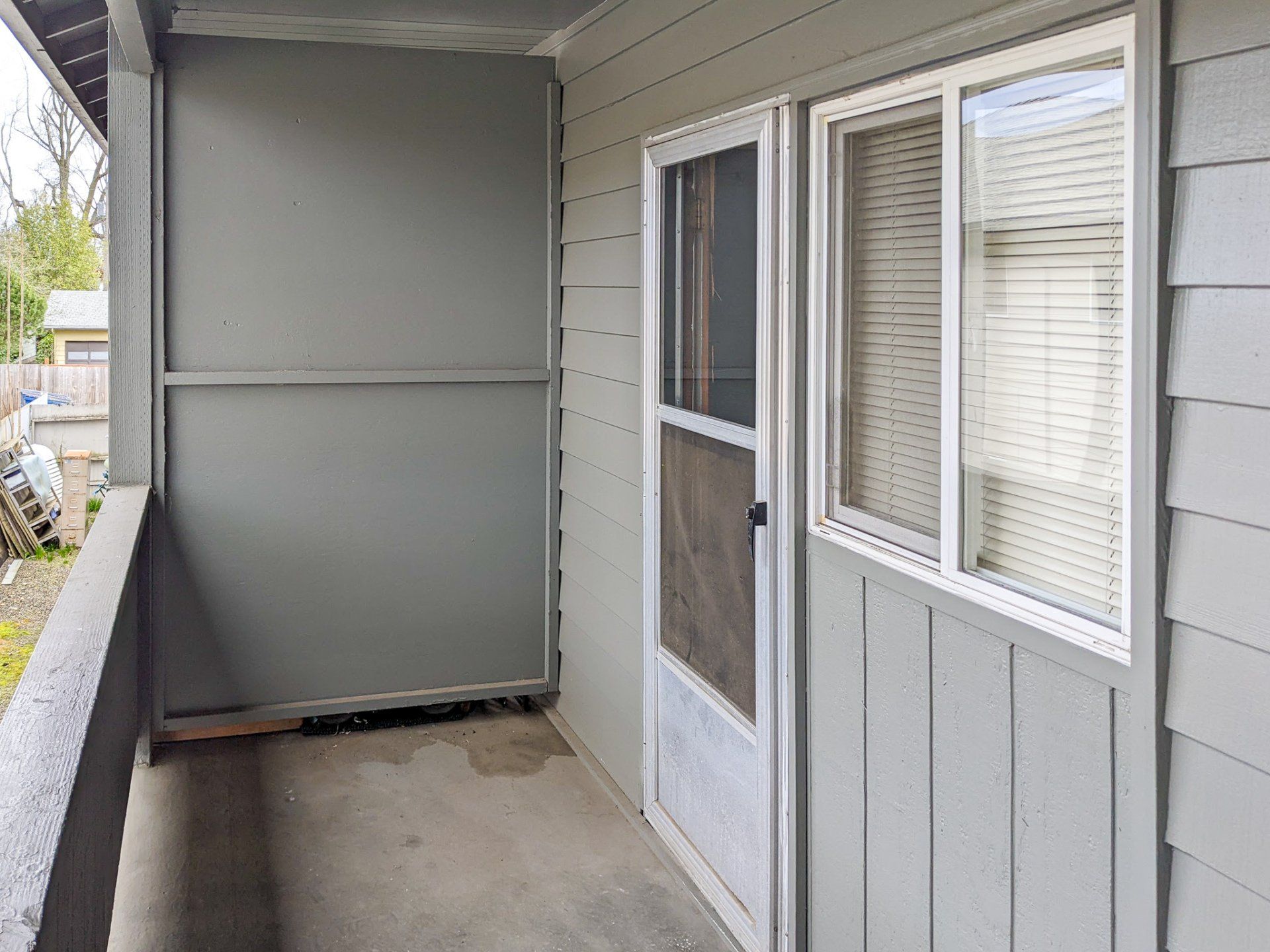 A balcony with a screen door and a window on the side of a house.