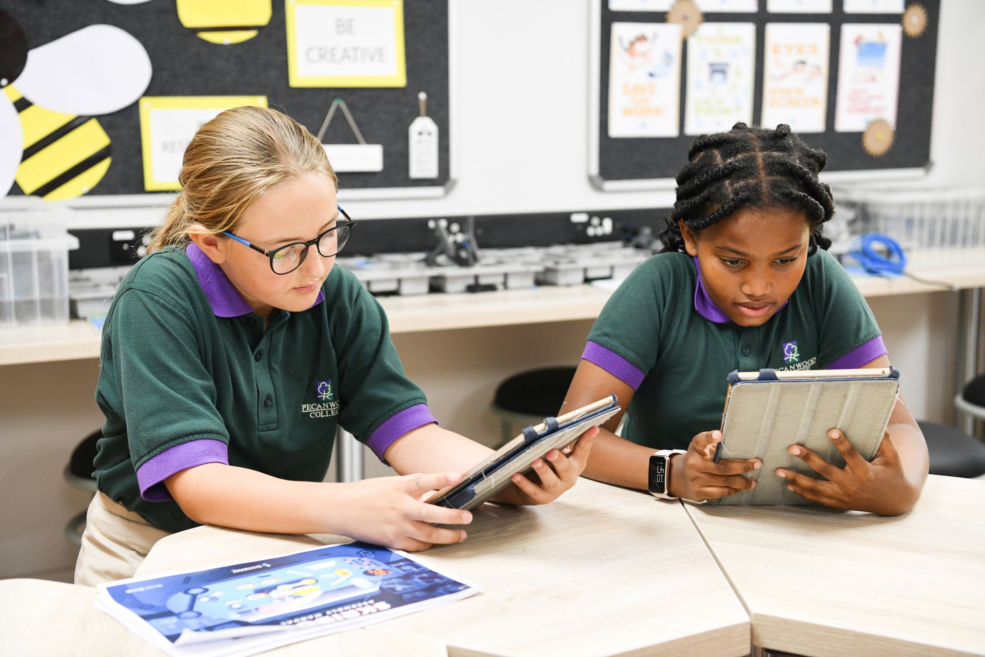 two young girls are sitting at a table looking at a tablet .