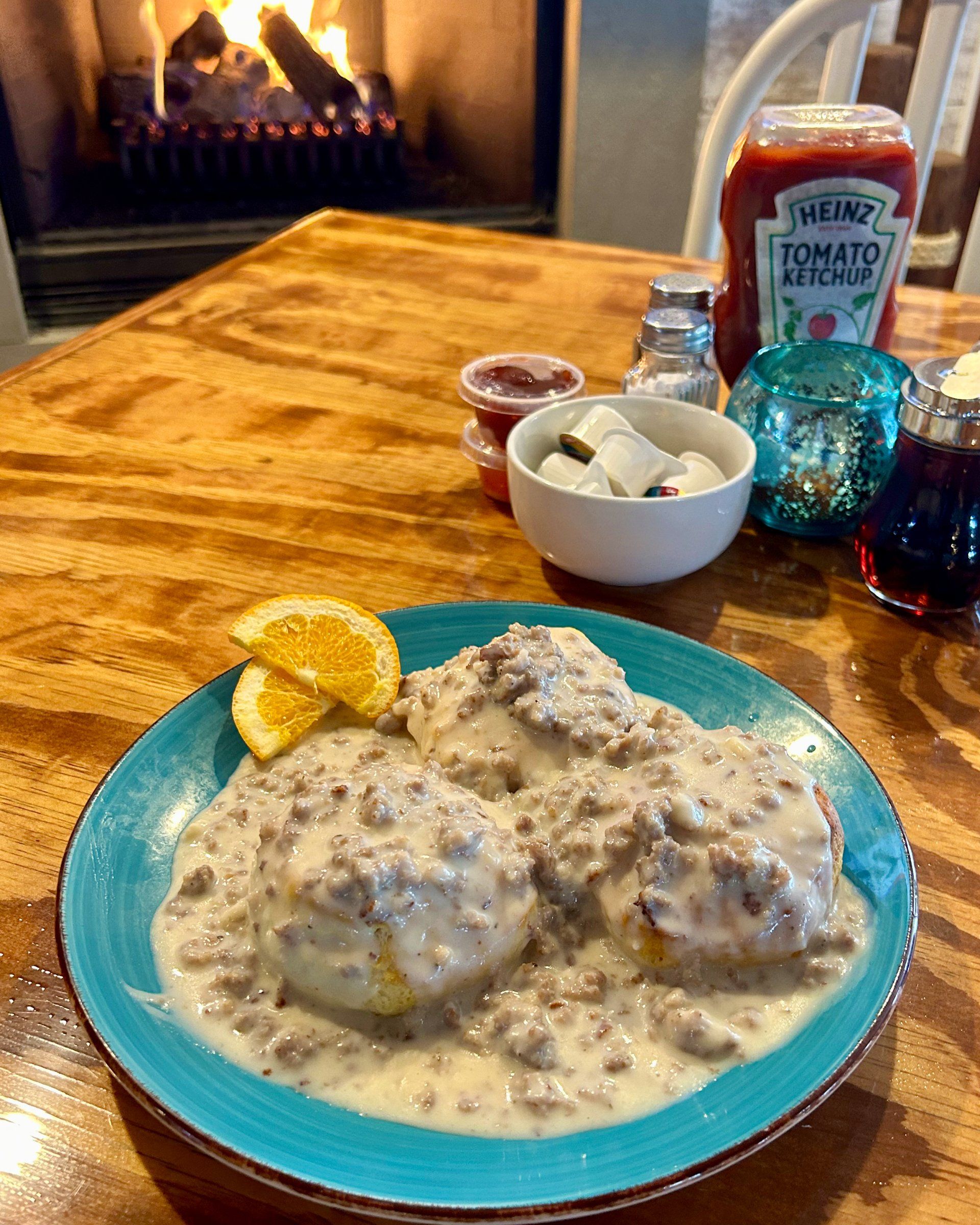 A plate of biscuits and gravy with a slice of orange on a wooden table.
