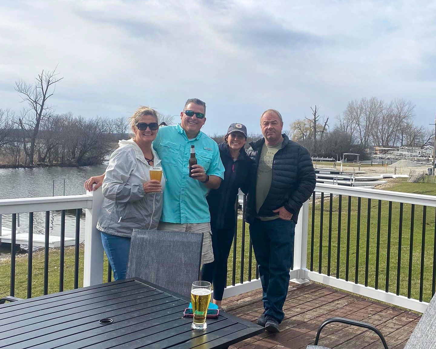 A group of people are standing on a deck holding beer bottles.