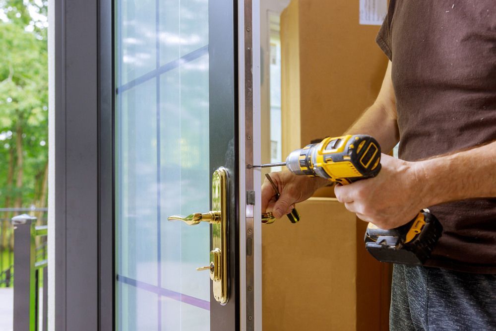 A Man Is Fixing A Door With A Drill — Grafton Locksmith Service In Grafton, NSW