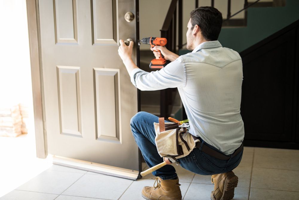 A Man Is Fixing A Door With A Drill — Grafton Locksmith Service In Grafton, NSW