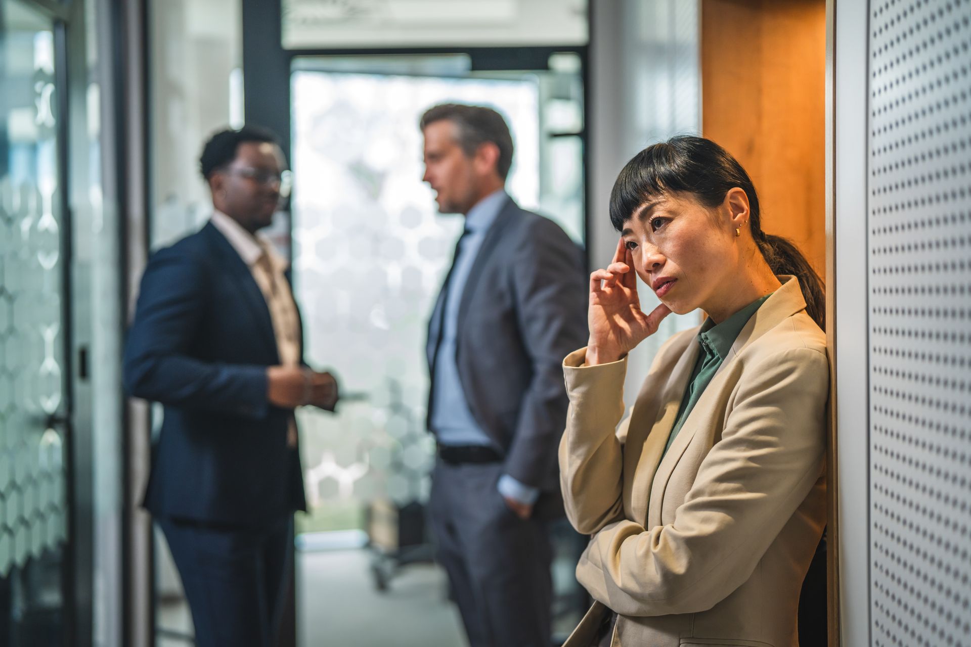 Female employee experiencing exclusion in a workplace with two coworkers in the background.