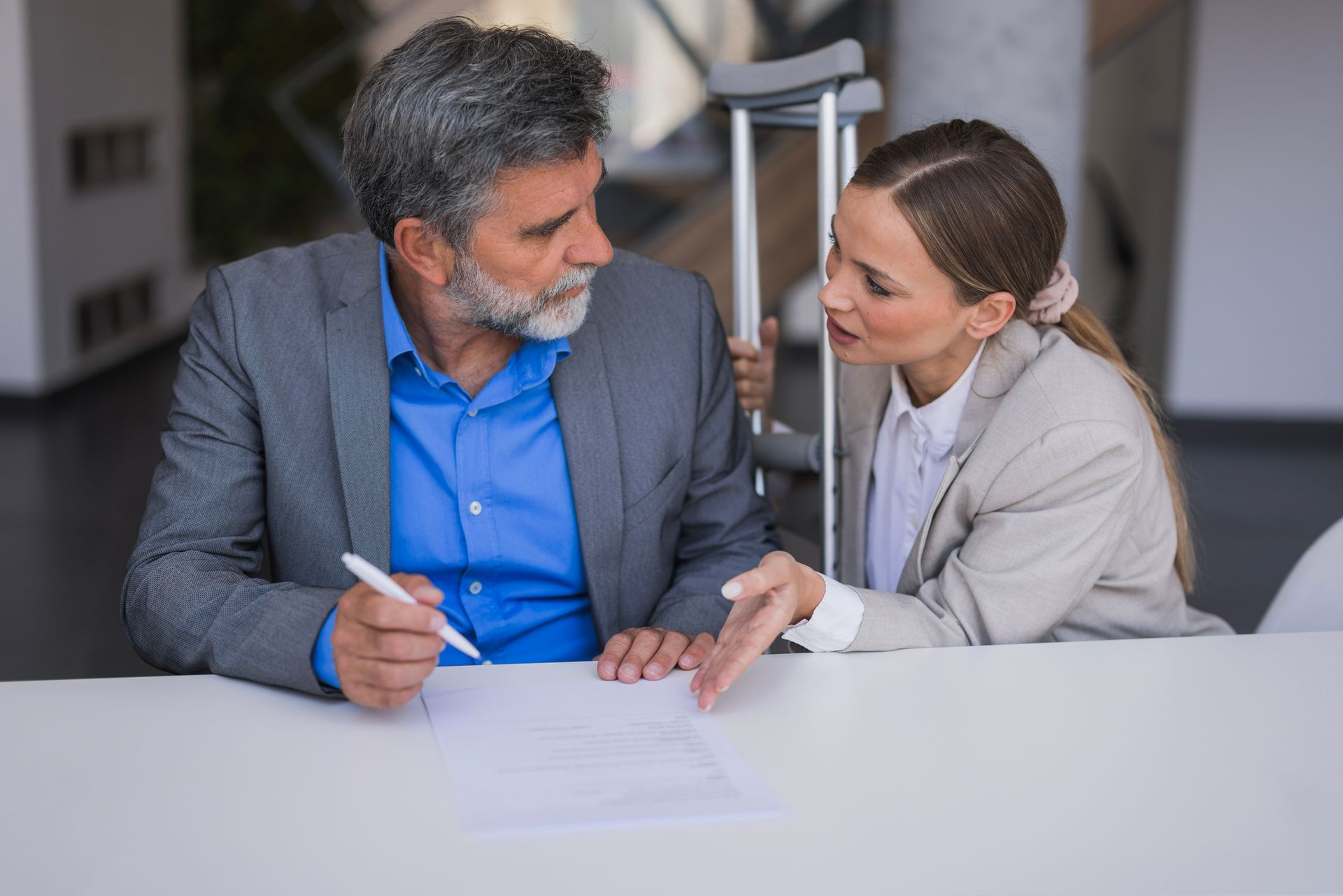 A man with crutches speaks with a female injury claim attorney inside an office. A man with crutches speaks with a female injury claim attorney inside an office.