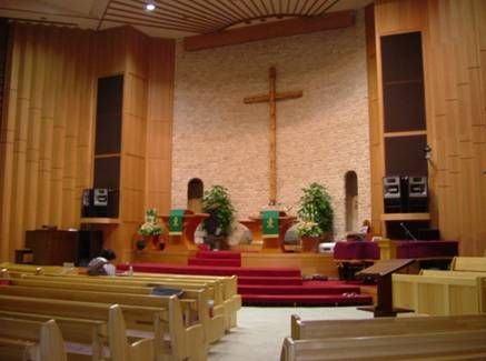 Church altar featuring a stone wall, tall wooden cross, and speaker stacks.