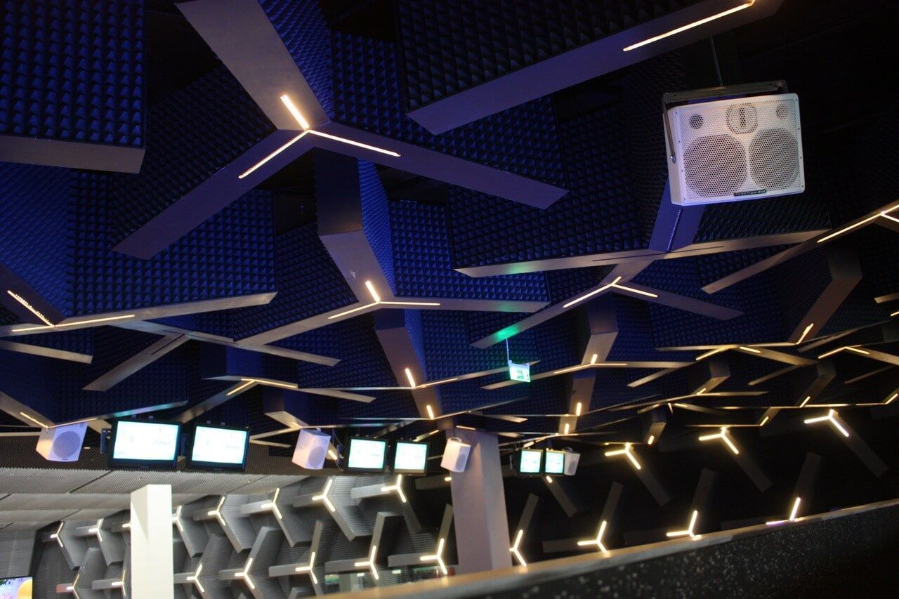 Stylish bar interior featuring futuristic ceiling lights, wall patterns, and mounted speakers for a premium audio experience.
