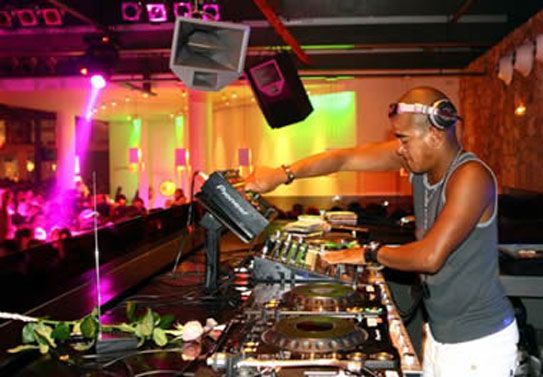 A DJ performing live in a nightclub with colorful lights and a party crowd