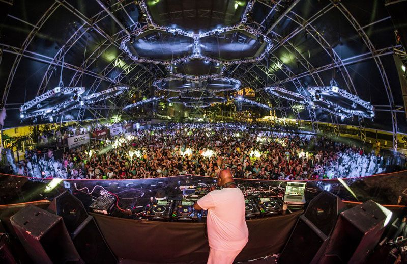 Massive crowd at nighttime EDM festival under a dome with circular light rigs.