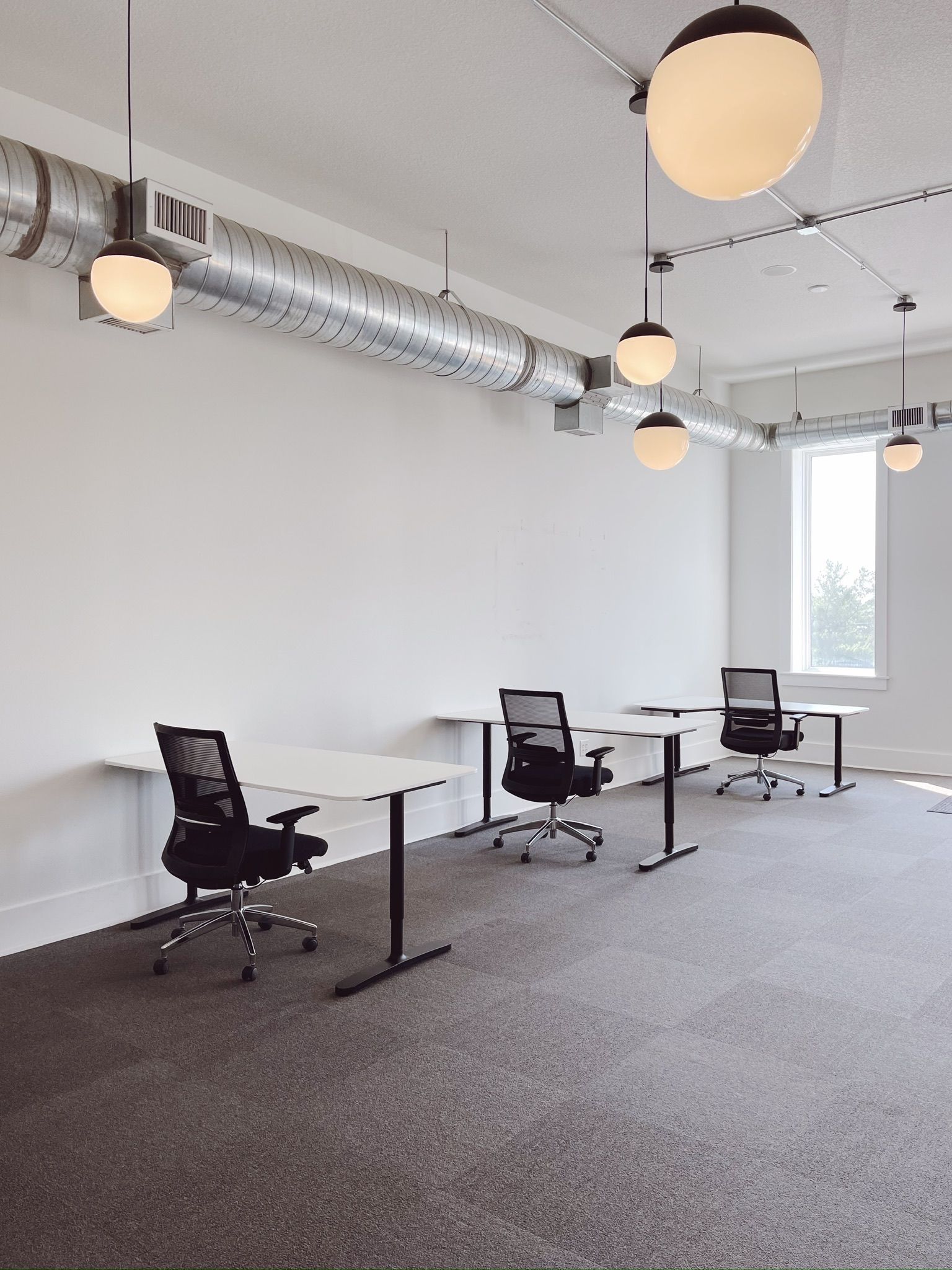 Empty modern office with desks, swivel chairs, large windows, and hanging globe lights