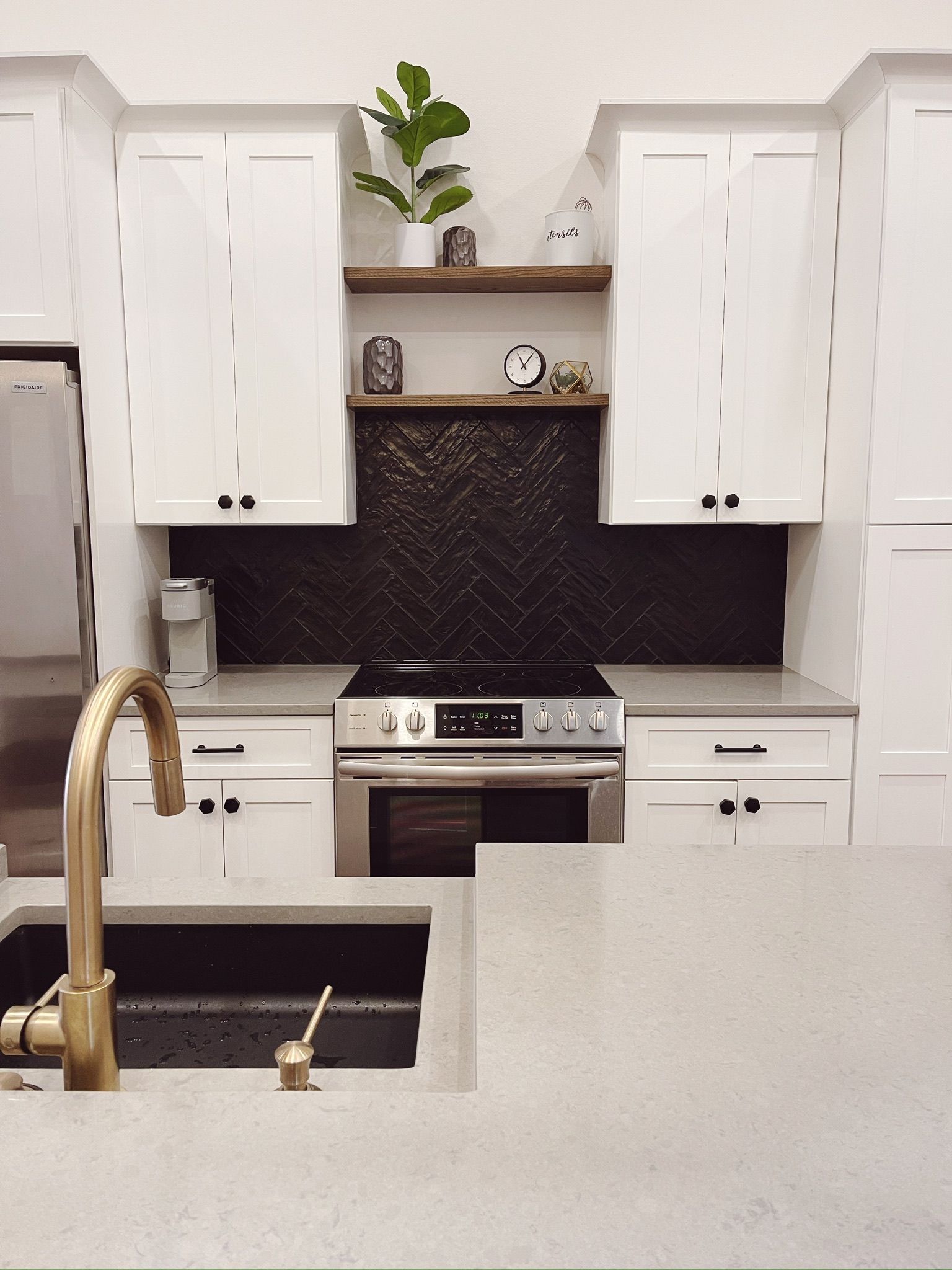 Modern white kitchen with gold faucet, stainless stove, and open shelves with plants and decor