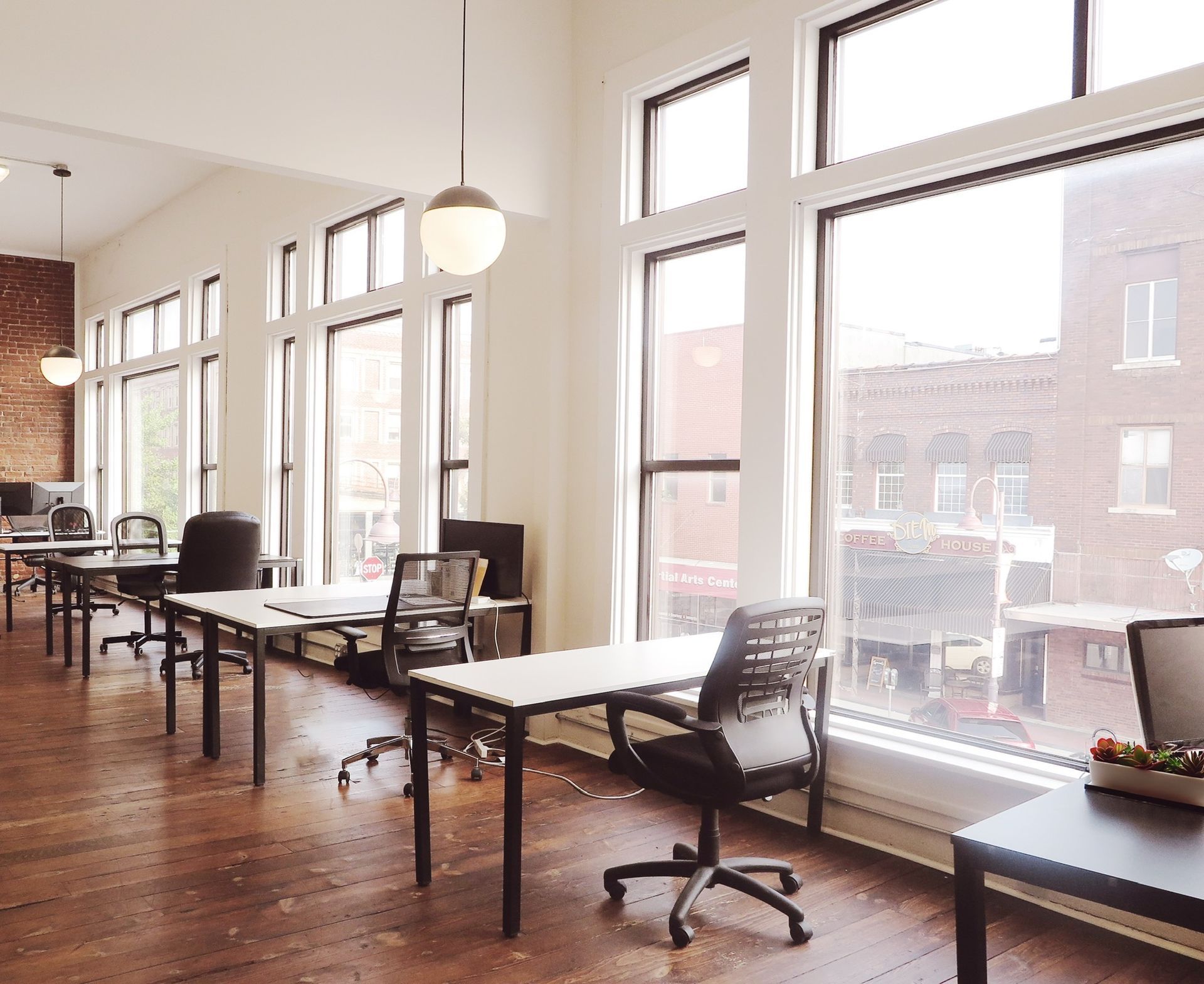 Bright modern office with desks, chairs, large windows, and hardwood floors.