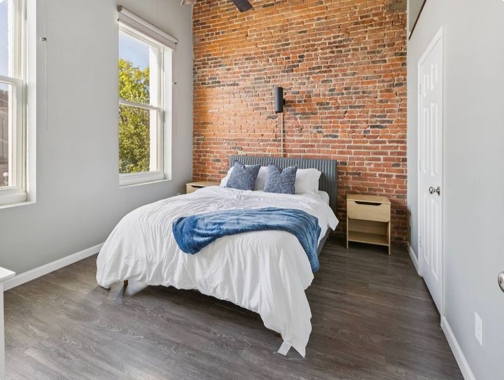 Bright bedroom with exposed brick wall, white bed, and dark wood floor