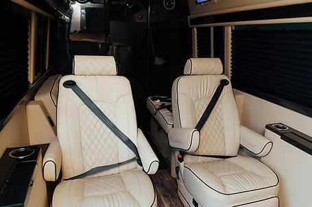 Inside of a luxury van with two cream-colored leather seats, seatbelts, and drink holders. Inside of a luxury van with two cream-colored leather seats, seatbelts, and drink holders.